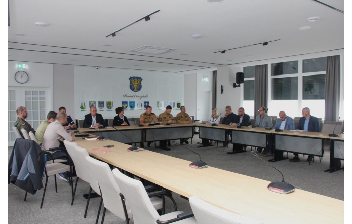 W sali konferencyjnej Starostwa w Cieszynie przy długim stole obradują przedstawiciele służb mundurowych, instytucji i samorządu, skupieni na dyskusji. W tle herb powiatu i godła gmin.