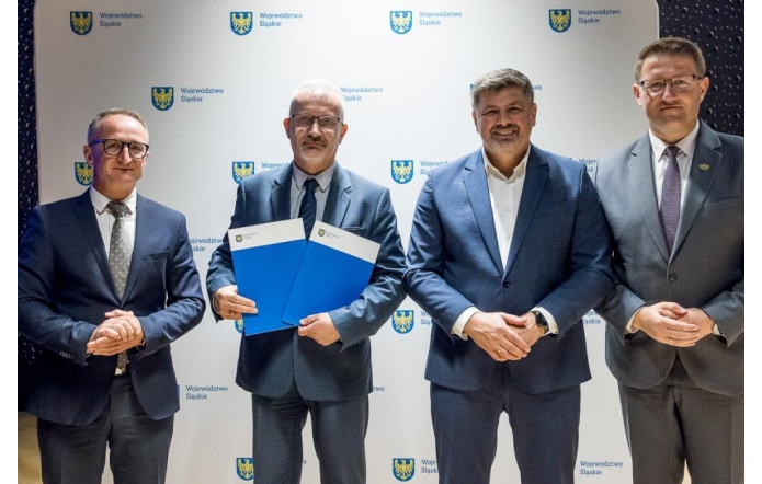 Czterech mężczyzn w garniturach pozuje do zdjęcia na tle ścianki z logotypami Województwa Śląskiego.