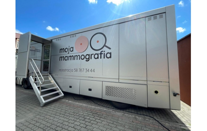 Mobilna pracownia mammograficzna w formie dużej, jasnej naczepy z logo „moja mammografia”, z metalowymi schodkami prowadzącymi do wejścia i numerem telefonu do rejestracji na boku pojazdu.